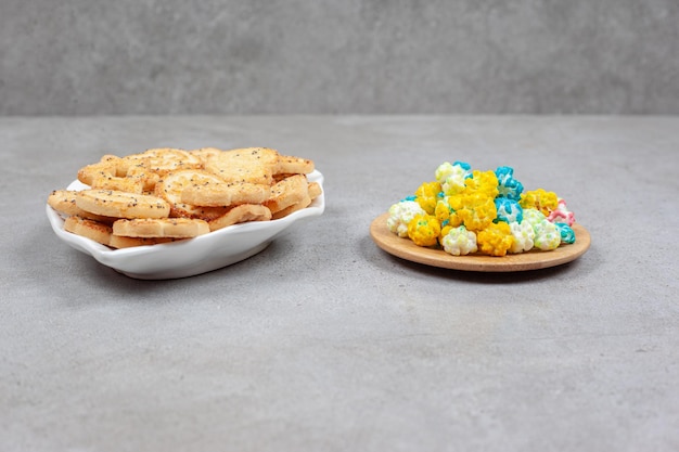 Biscotti su un piatto decorato accanto a un piccolo vassoio in legno di caramelle popcorn su una superficie di marmo.