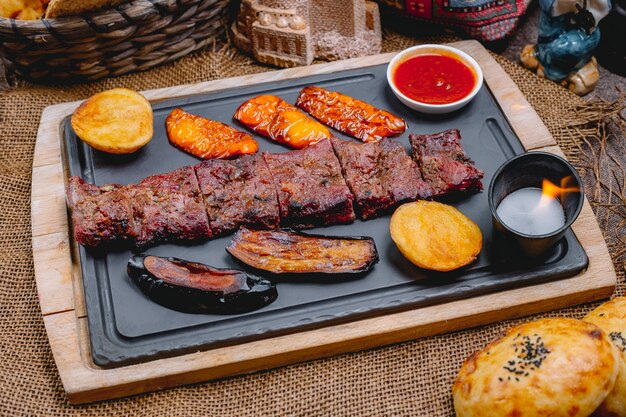 Bistecca alla griglia di vista laterale con pane e candela della salsa del peperone dolce delle patate della melanzana su un bordo