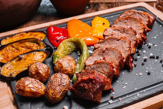 Bistecca arrostita affettata sulla vista laterale del peperone dolce della patata della melanzana del bordo di legno