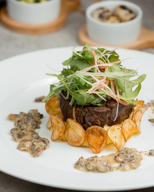 Bistecca di carne con insalata verde e patatine fritte.