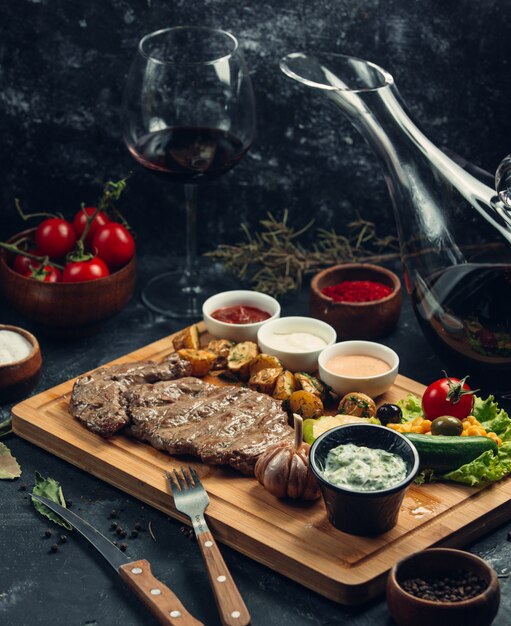 Bistecca di carne con verdure e varietà di salse su una tavola di legno.