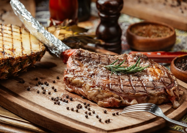 Bistecca di carne su un piatto di legno con pepe nero e rosmarino.