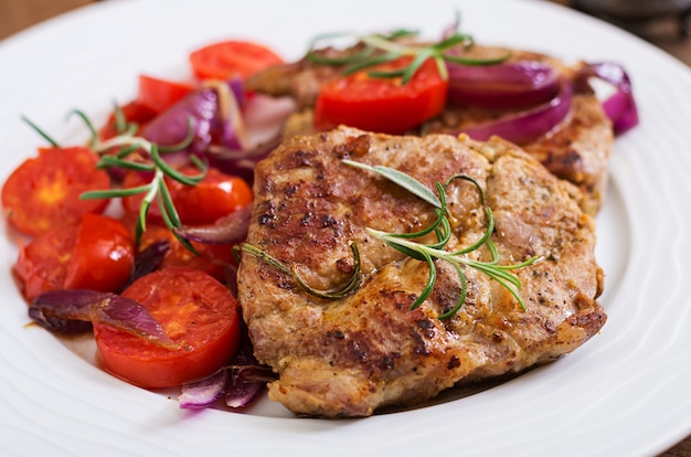 Bistecca di maiale succosa con rosmarino e pomodori su un piatto bianco