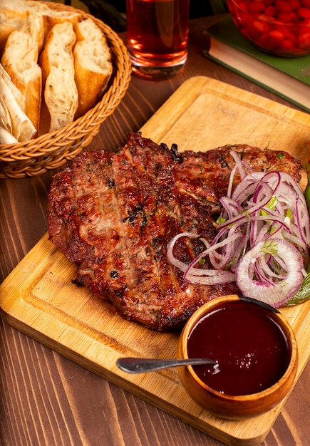 Bistecca di manzo con barbecue, salsa barbecue ed erbe aromatiche, insalata di cipolle, pepe alla griglia e pomodoro sul piatto di legno