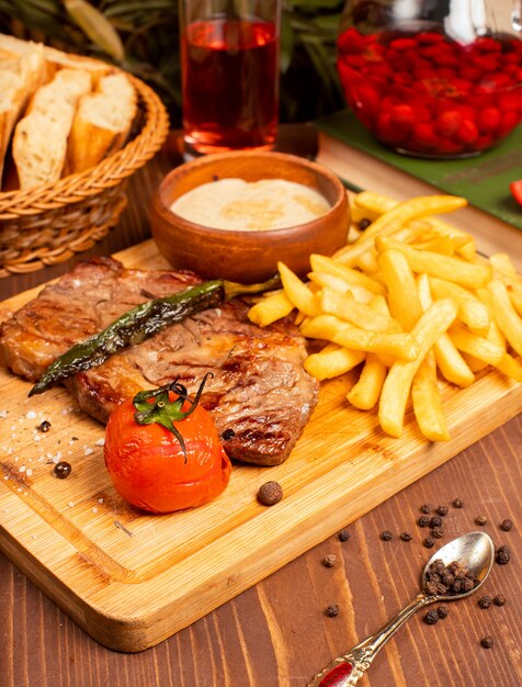 Bistecca di manzo con patatine fritte, salsa di maionese panna acida ed erbe sul piatto di legno