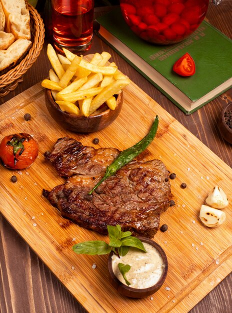 Bistecca di manzo con patatine fritte, salsa di maionese panna acida ed erbe sul piatto di legno