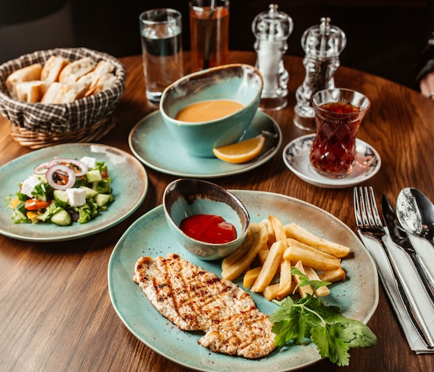 Bistecca di pollo con patatine fritte e ketchup servita con zuppa e insalata di verdure