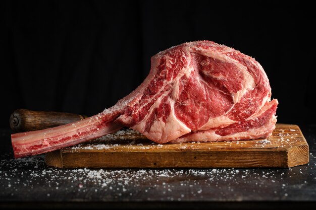 Bistecca di tomahawk della carne fresca sul bordo di legno vecchio. Sfondo scuro. Avvicinamento