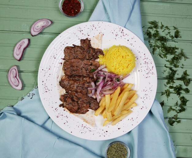 Bistecche di carne con patate fritte e contorno di riso all'interno del piatto bianco