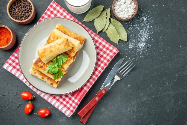 Blini ripieni di carne vista dall'alto su piastra rotonda foglie di alloro forchetta limone sul tavolo