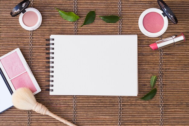 Blocchetto per appunti a spirale in bianco circondato con i prodotti cosmetici su placemat