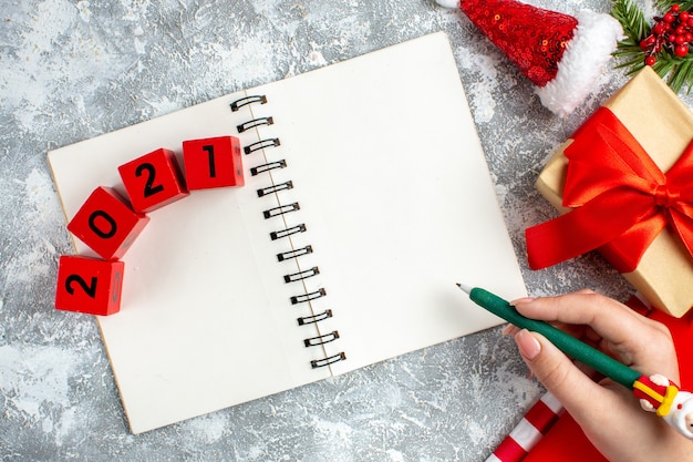 Blocchi di legno per notebook vista dall'alto piccolo cappello da Babbo Natale matita verde in mano femminile su tavolo grigio bianco