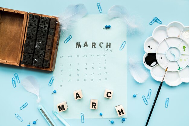 Blocchi tipografici in legno; piuma; marzo marcia e timbro marzo sul calendario con elementi decorativi su sfondo blu