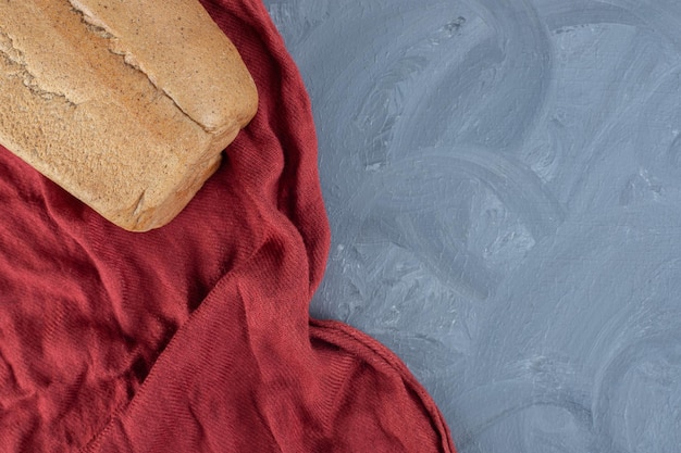 Blocco di pane sulla tovaglia rossa rugosa sul tavolo di marmo.