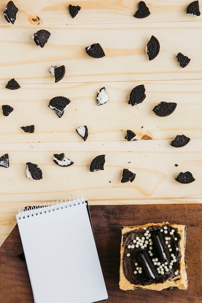 Blocco note con pasticceria vicino a pezzi di biscotti sul tavolo di legno