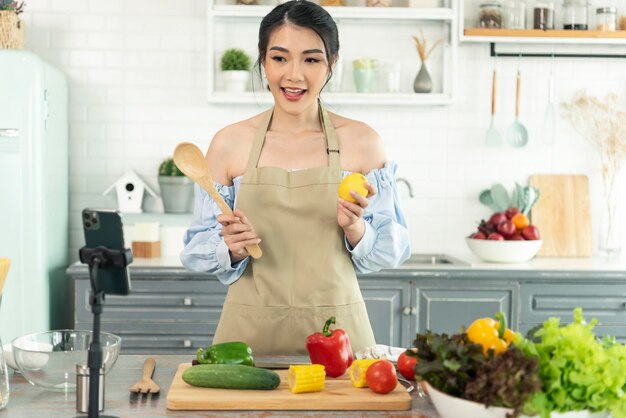 Blogger alimentare donna asiatica che cucina insalata davanti alla fotocamera dello smartphone durante la registrazione di video vlog