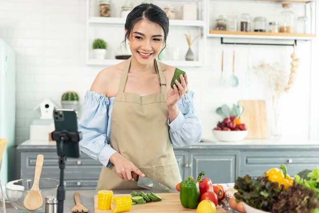 Blogger alimentare donna asiatica che cucina insalata davanti alla fotocamera dello smartphone durante la registrazione di video vlog