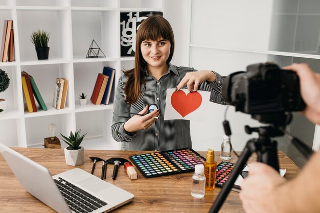 Blogger di trucco femminile con streaming con fotocamera e laptop a casa