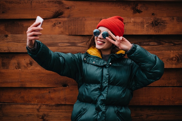 Blogger donna elegante in abito multicolore brillante fa selfie sulla parete di legno