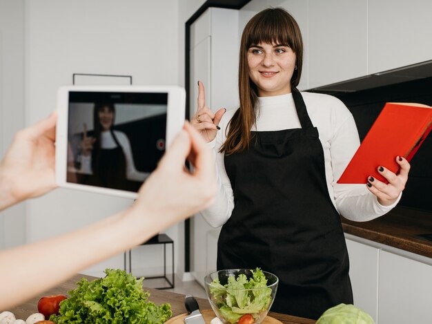 Blogger femminile che si registra mentre prepara insalata e libro di lettura