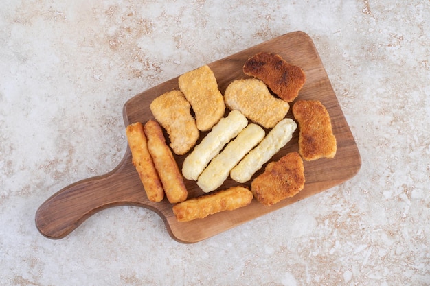 Bocconcini di pollo classici, salsiccia e bastoncini di formaggio su un piatto di legno.