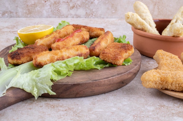 Bocconcini di pollo fritto e bastoncini di formaggio su una tavola di legno su un pezzo di foglia di lattuga.