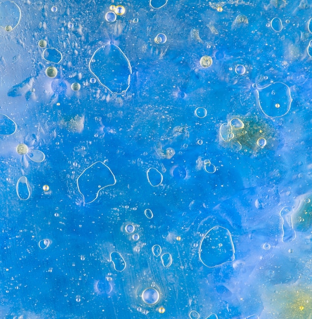Bolle d&#39;olio che galleggiano sulla superficie dell&#39;acqua blu