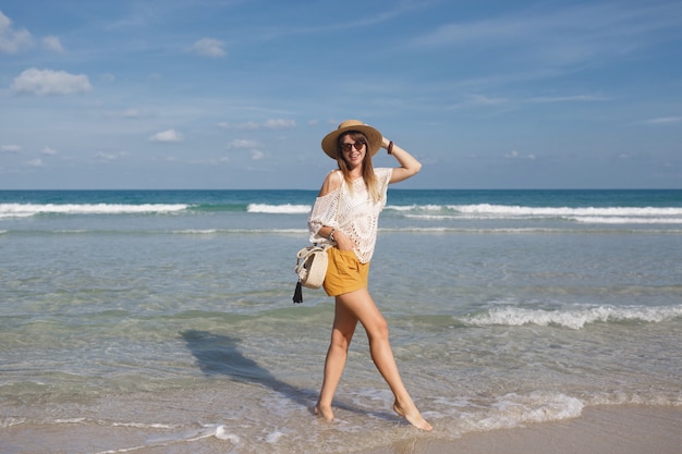 Borsa della paglia della tenuta della donna e camminare sulla spiaggia