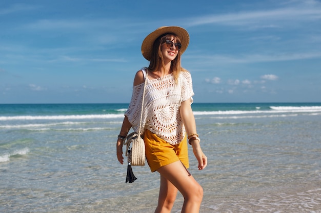 Borsa della paglia della tenuta della donna e camminare sulla spiaggia