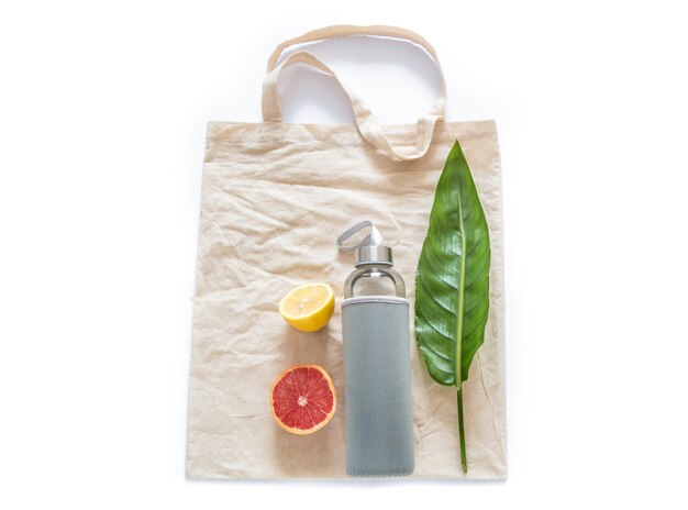 Borsa di cotone con bottiglia d'acqua frutta limoni crudi foglia verde sul muro bianco laici piatta. Zero rifiuti riutilizzabili materiali eco friendly senza plastica