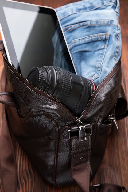 Borsa in pelle piena di jeans, macchina fotografica e tablet