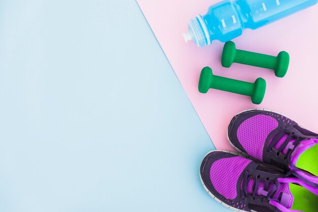 Bottiglia d&#39;acqua; scarpe sportive e manubri su sfondo rosa su sfondo blu