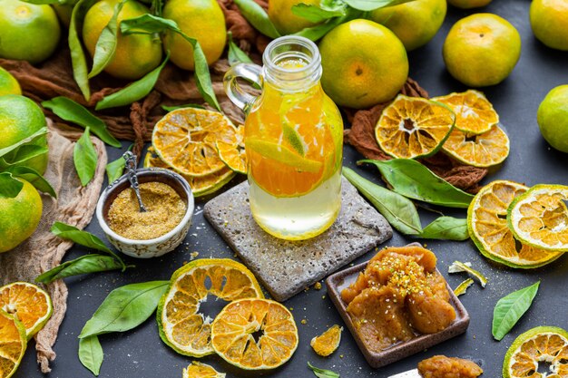 Bottiglia di acqua di mandarino su un tavolo circondato da polvere di mandarino e marmellata di agrumi secchi