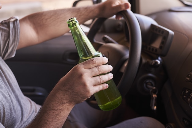 Bottiglia di birra nelle mani di un uomo che guida l'auto durante il giorno