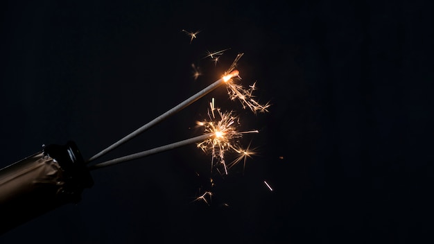 Bottiglia di Champagne con lo sparkler bruciante del fuoco su fondo nero