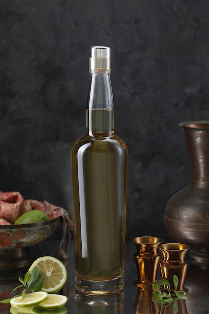 Bottiglia di liquore con mini calici, vaso, limone, sciarpa e foglie di menta