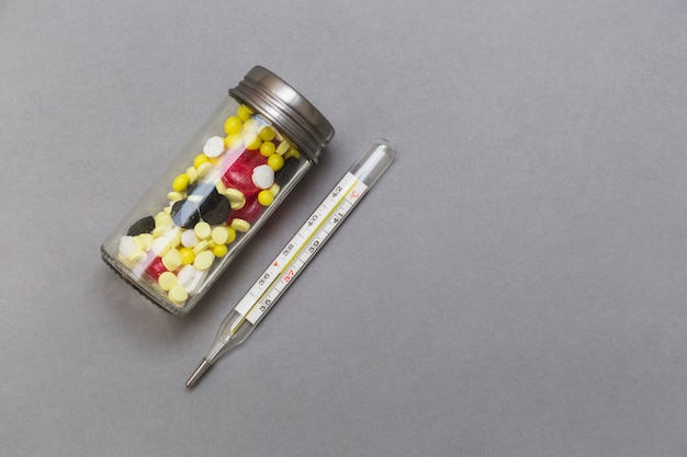 Bottiglia di pillole e termometro su sfondo grigio
