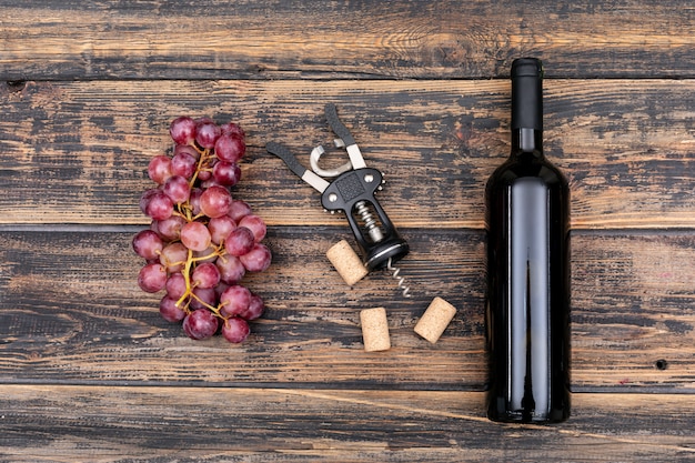 Bottiglia di vino di vista superiore con l'uva sull'orizzontale di legno scuro
