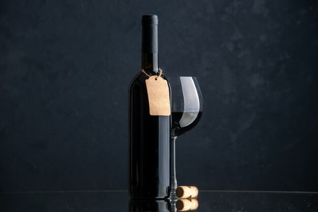 Bottiglie di vino di vista frontale con un bicchiere di vino sulla superficie scura