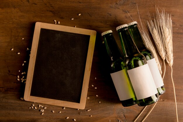 Bottiglie verdi con l&#39;etichetta e la lavagna bianche sulla tavola di legno