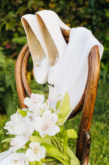 Bouquet di fiori da sposa; tacchi alti e sciarpa sulla sedia di legno nel parco