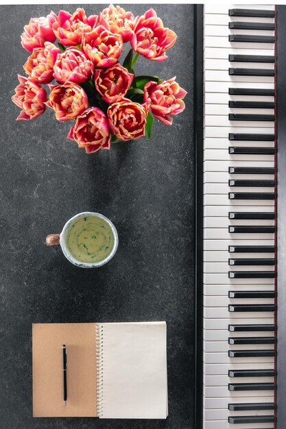 Bouquet di fiori di primavera per pianoforte, blocco appunti e tazza di tè su uno sfondo scuro