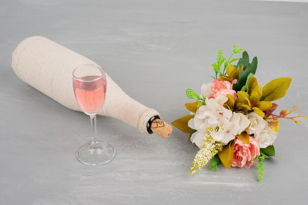 Bouquet di fiori e un bicchiere di vino rosato sulla superficie grigia