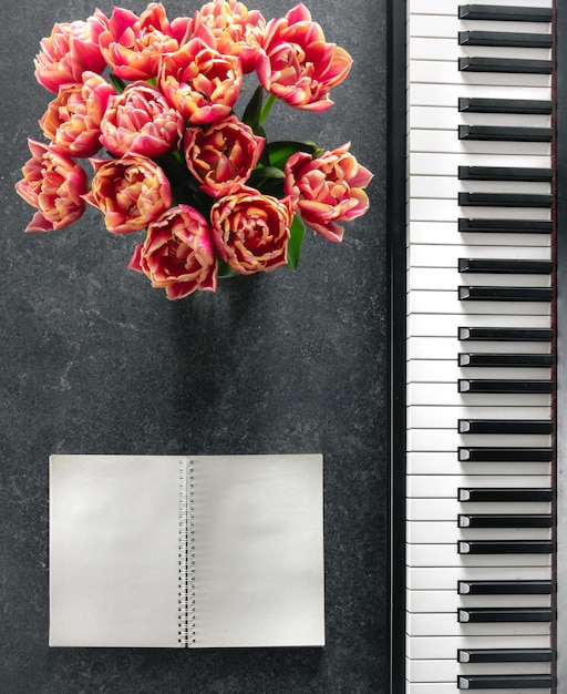 Bouquet di pianoforte di fiori di tulipano e blocco note su uno sfondo scuro vista superiore