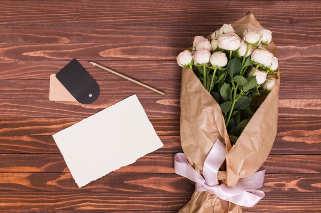 Bouquet di rose bianche; foglio bianco; matita e cartellino del prezzo su sfondo in legno