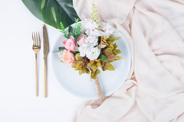 Bouquet di rose, posate e piatto sulla superficie bianca.