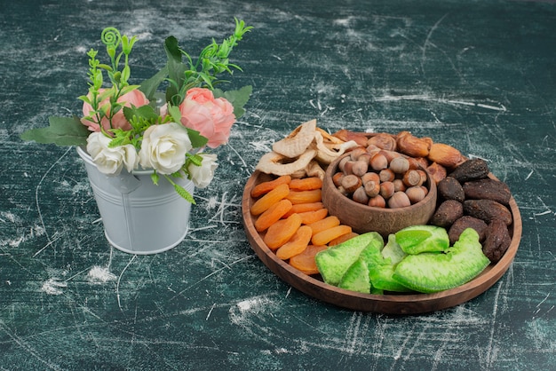 Bouquet minuscolo con piatto in legno di frutta secca su superficie in marmo.