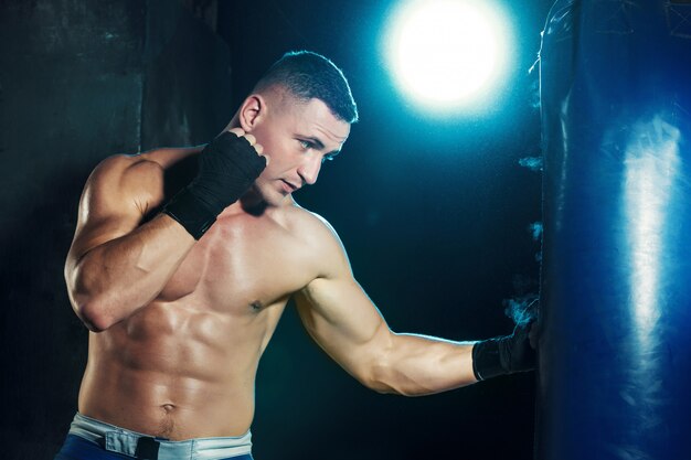 Boxer maschio nel sacco da boxe con drammatica illuminazione tagliente
