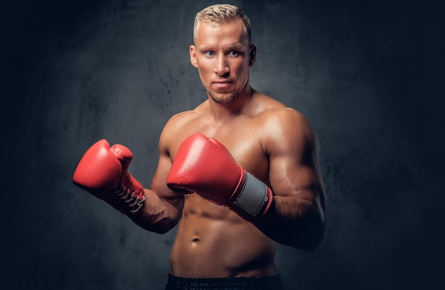 Boxer senza camicia che mostra i suoi pugni e calci su sfondo grigio in uno studio.