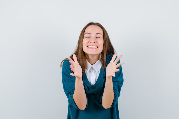 Braccia di apertura della giovane donna per l'abbraccio in maglione sopra la camicia bianca e guardando felice, vista frontale.